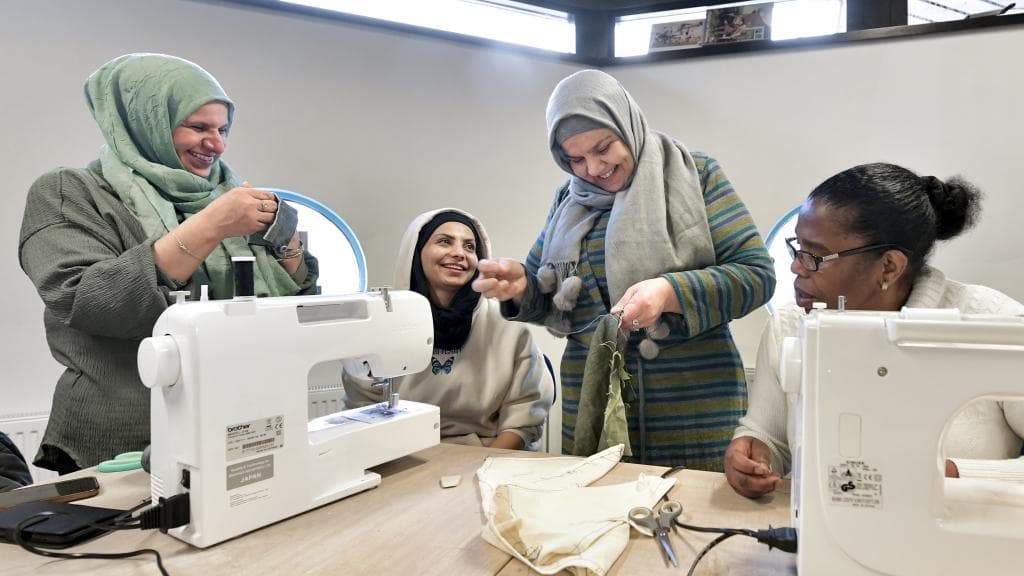 Vier vrouwen zijn bezig met naaimachines en lachen.