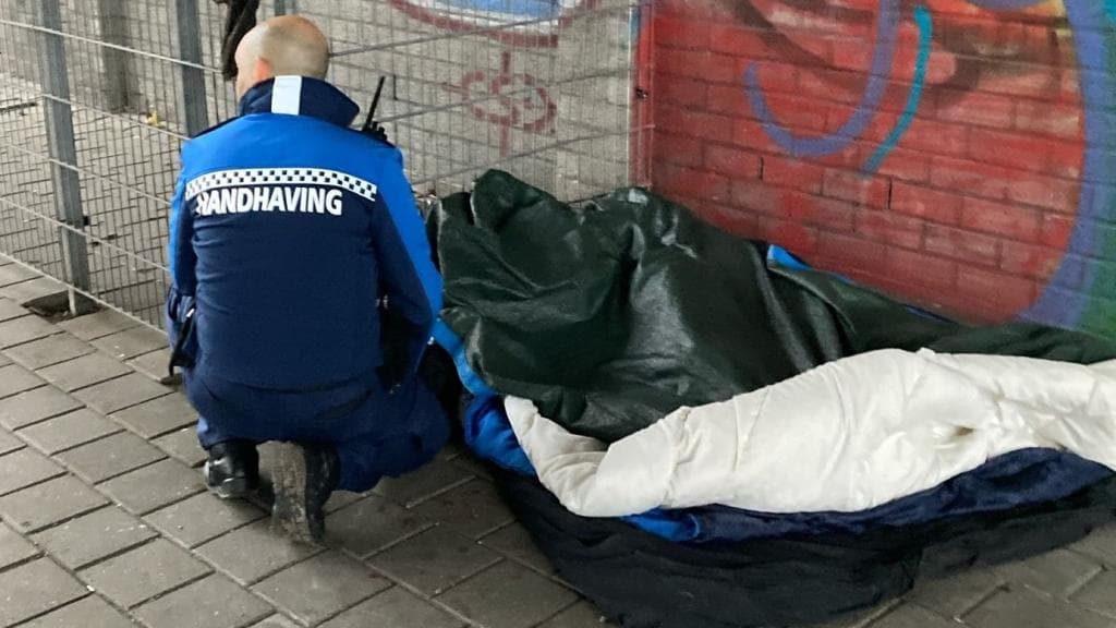 Een handhaver knielt naast een slaapplek op straat.