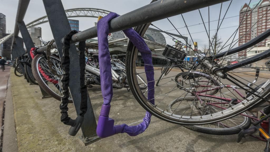 Fiets vastgemaakt met een paarse ketting aan een hek. Erachter ligt een omgevallen fiets. Foto: gemeente Rotterdam.