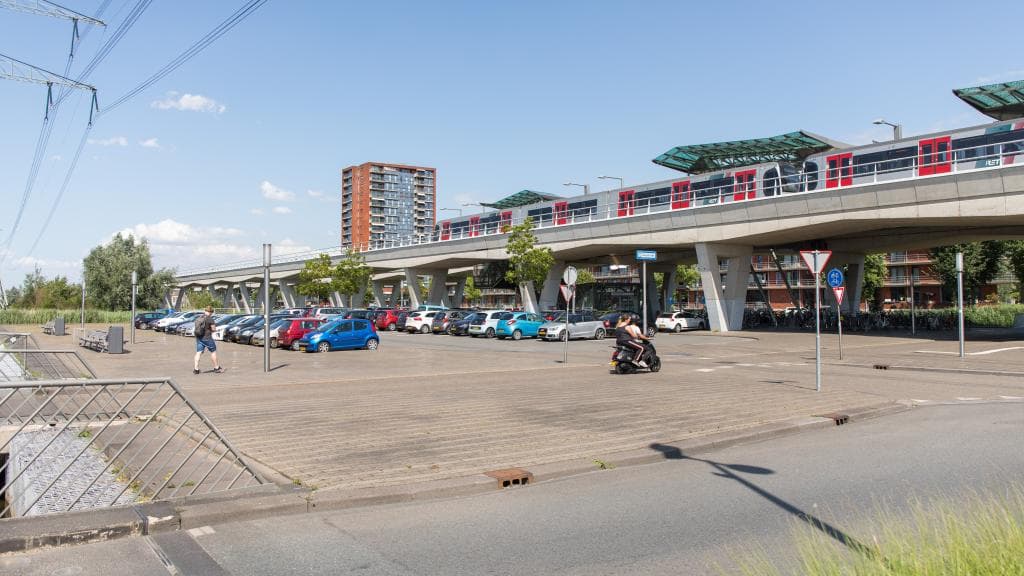 Geparkeerde auto's bij P+R Nesselande met rijdende brommer en voetganger op de voorgrond