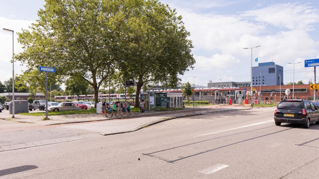Geparkeerde auto's bij P+R Schenkel met lopende kinderen, een stilstaande auto en metrostation op de achtergrond