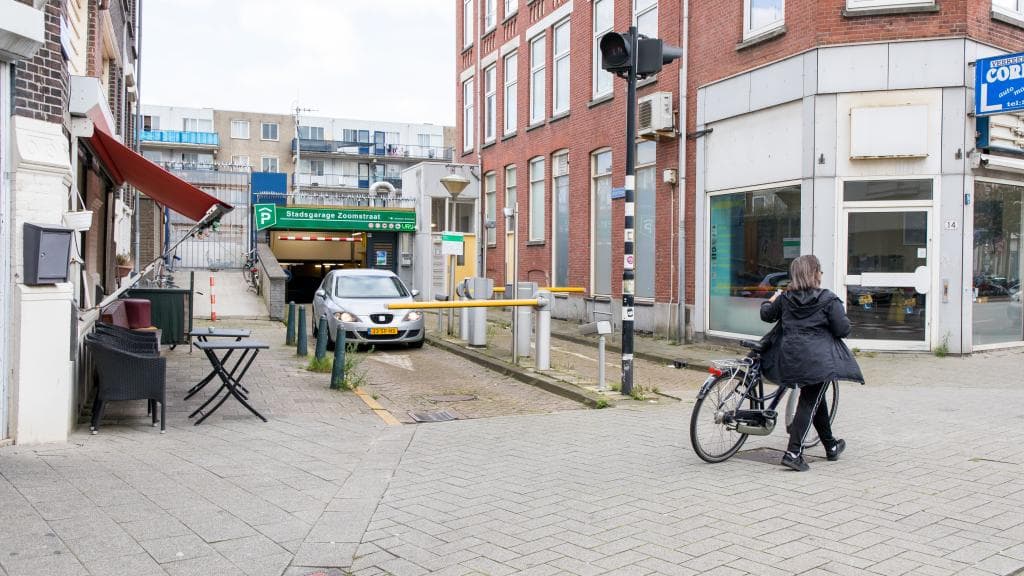 ingang parkeergarage en voetganger met fiets aan de hand en een grijze auto