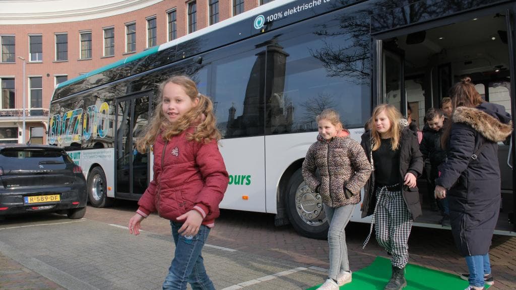 Kinderen komen uit een bus waarop staat: 100% elektrische touringcar