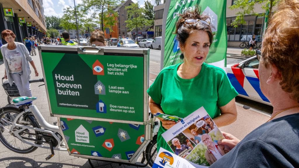 Voorlichter Lia van den Hoek staat met haar groene 'Houd boeven buiten' bakfiets op straat en deelt folders uit aan voorbijgangers.