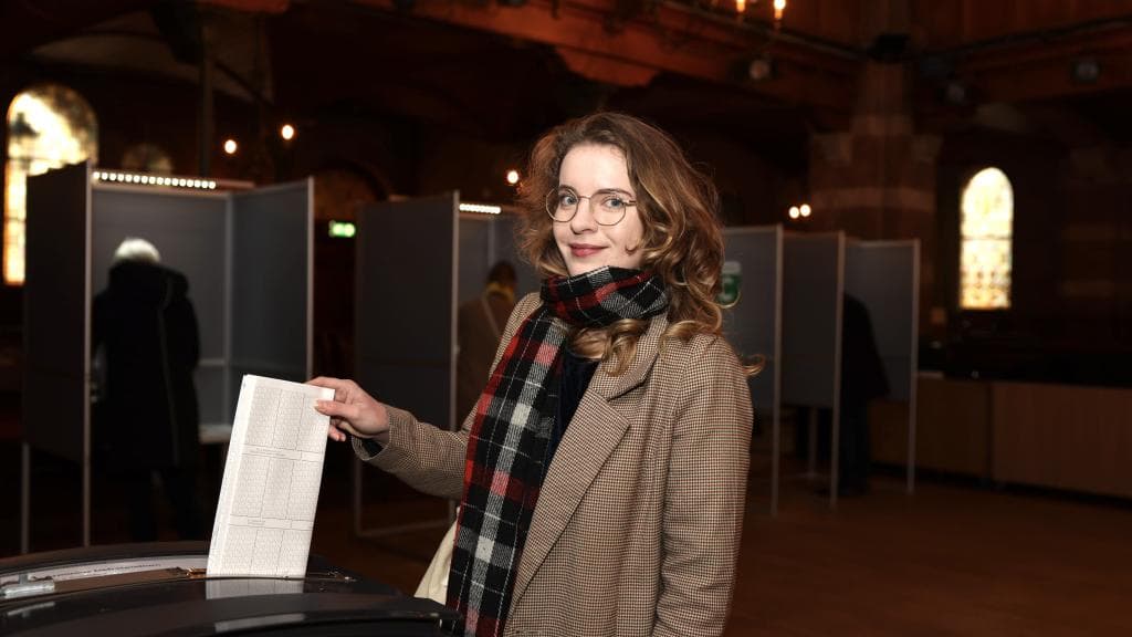 Een vrouw stopt een stembiljet in een stembus.